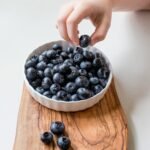 person holding bowl of black berries